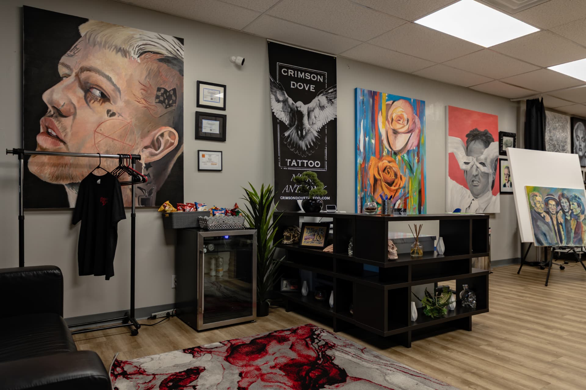 Crimson Dove Tattoo reception and waiting area with a black leather sofa, a patterned rug, and a Crimson Dove Tattoo banner on the wall