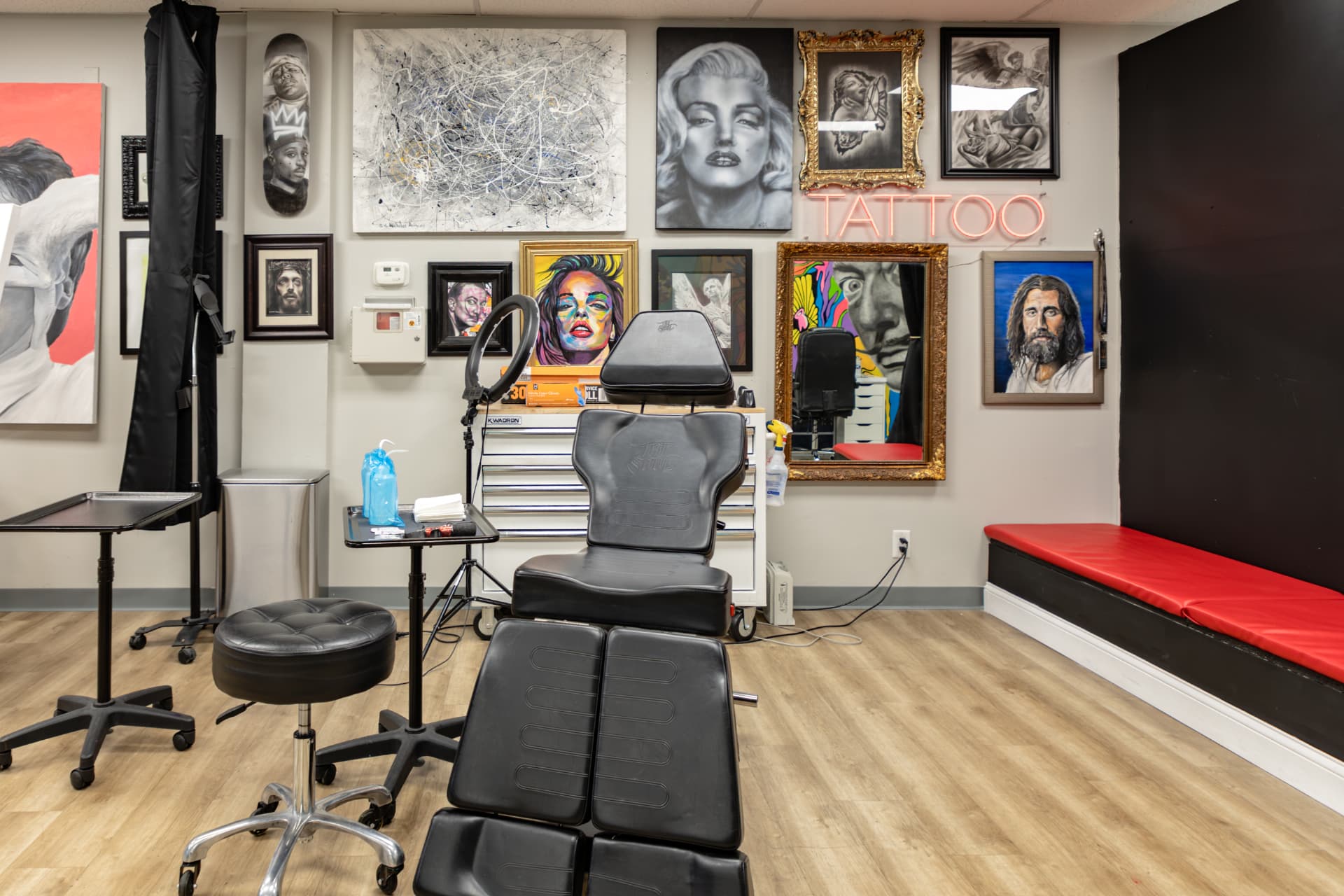 Tattoo station at Crimson Dove Tattoo with a black leather chair, instrument trays, and a neon sign on an art wall